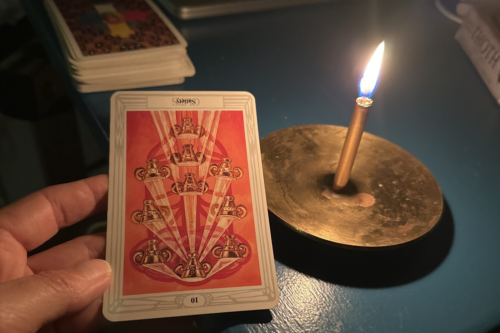 A Thoth tarot card held beside a lit candle in a brass holder